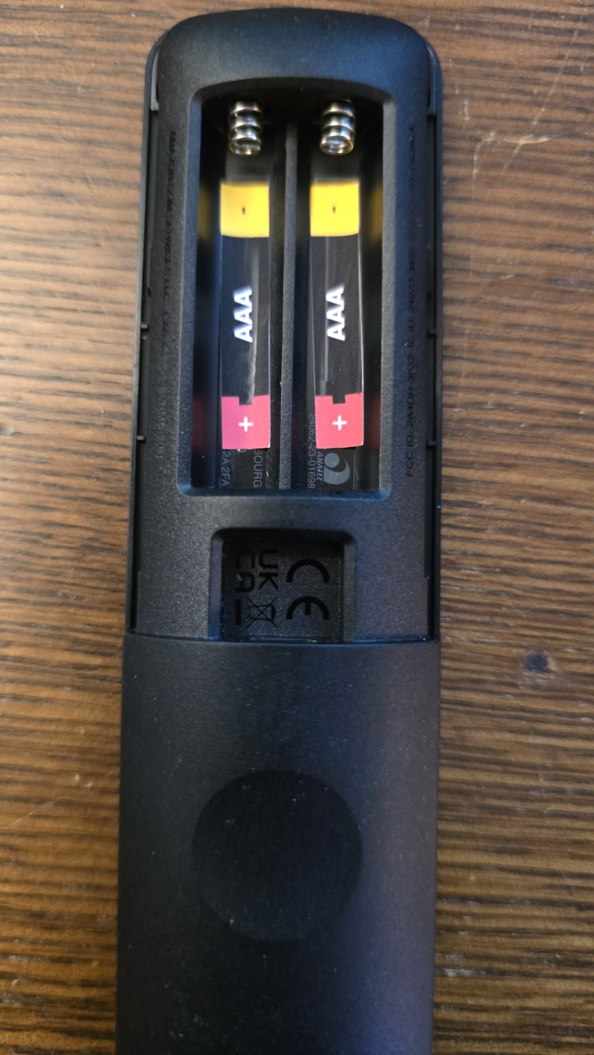 Portrait photo of a remote control with the battery compartment open and BatteryBright AAA labels visible